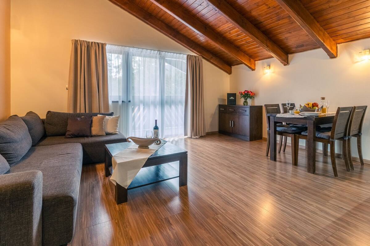 A modern living room with a wooden ceiling, a sofa, a dining table with chairs, and a kitchen area.