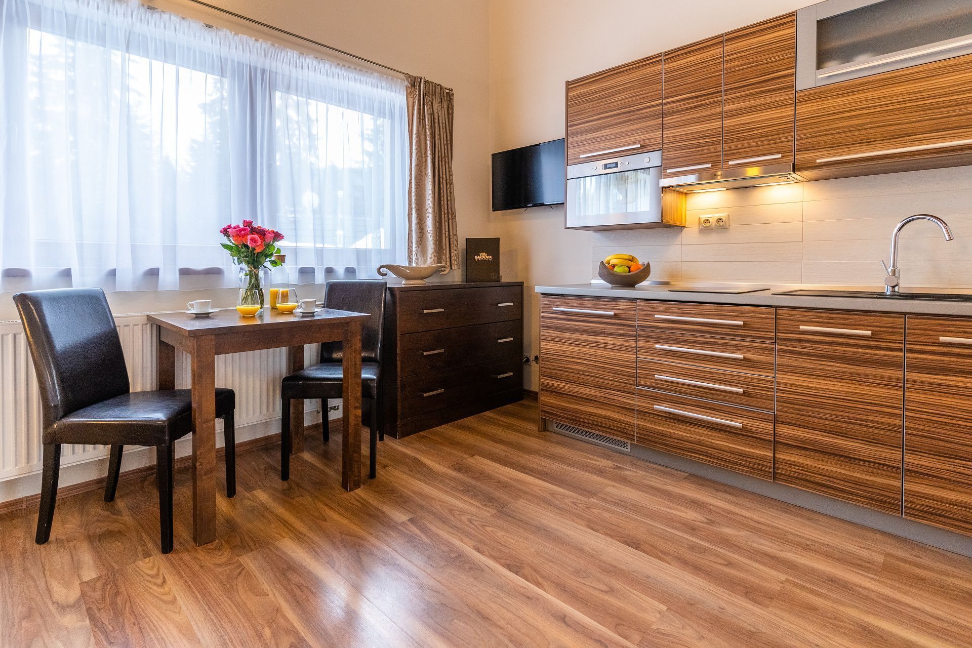 A modern kitchen with wooden cabinets, a built-in microwave, and a large window with sheer curtains.