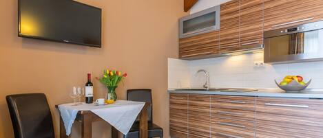 A modern kitchen with wooden cabinetry, a built-in microwave, and a large flat-screen TV mounted on the wall.