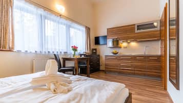 A hotel room with a bed, a desk, a chair, a small kitchenette, and a TV.