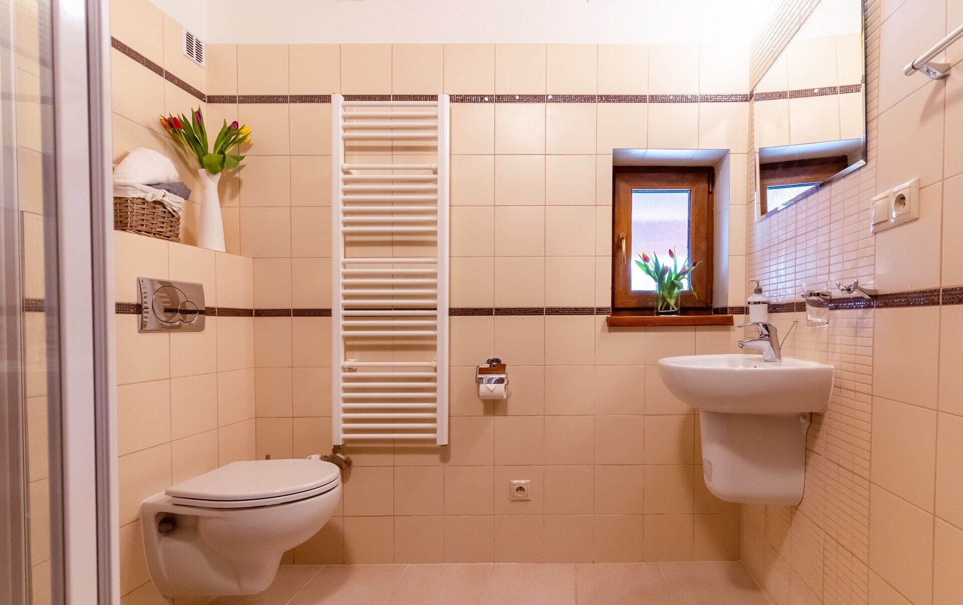 A bathroom with a toilet, bidet, and sink, a towel rack, a window with a view, and a towel dispenser.