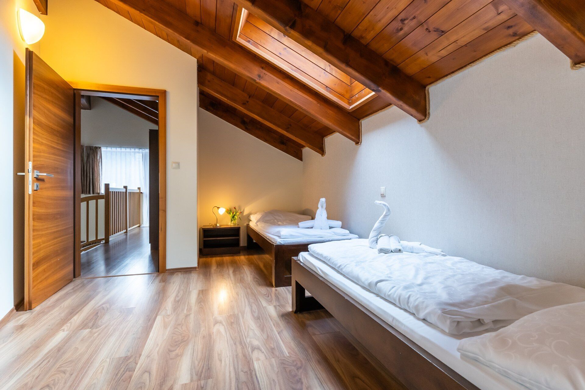 A bedroom with a wooden ceiling, a bed, a bedside table with a lamp, and a view of a balcony.