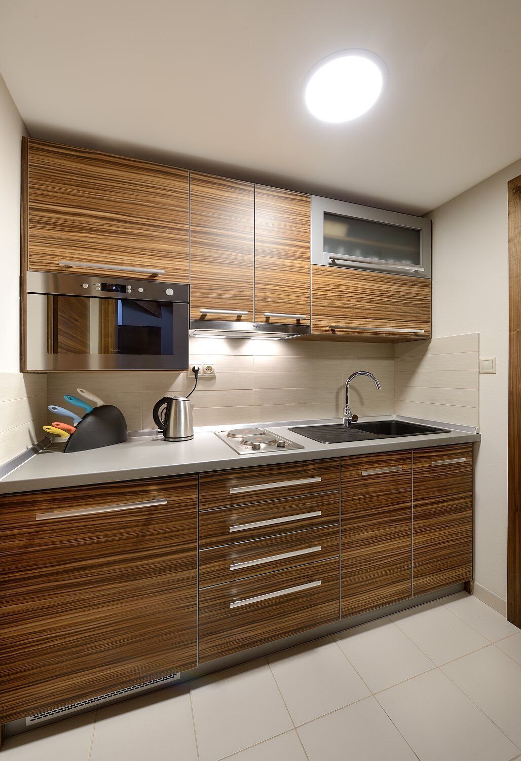 A modern kitchen with wooden cabinetry, a stainless steel oven, a built-in microwave, a sink, and a kettle.