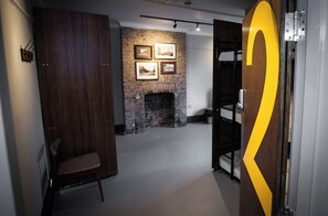 A room with a brick fireplace, wooden walls, a chair, bunk beds, and framed pictures on the wall.