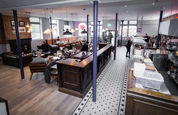 A modern restaurant with a bar area, seating, and a kitchen visible.