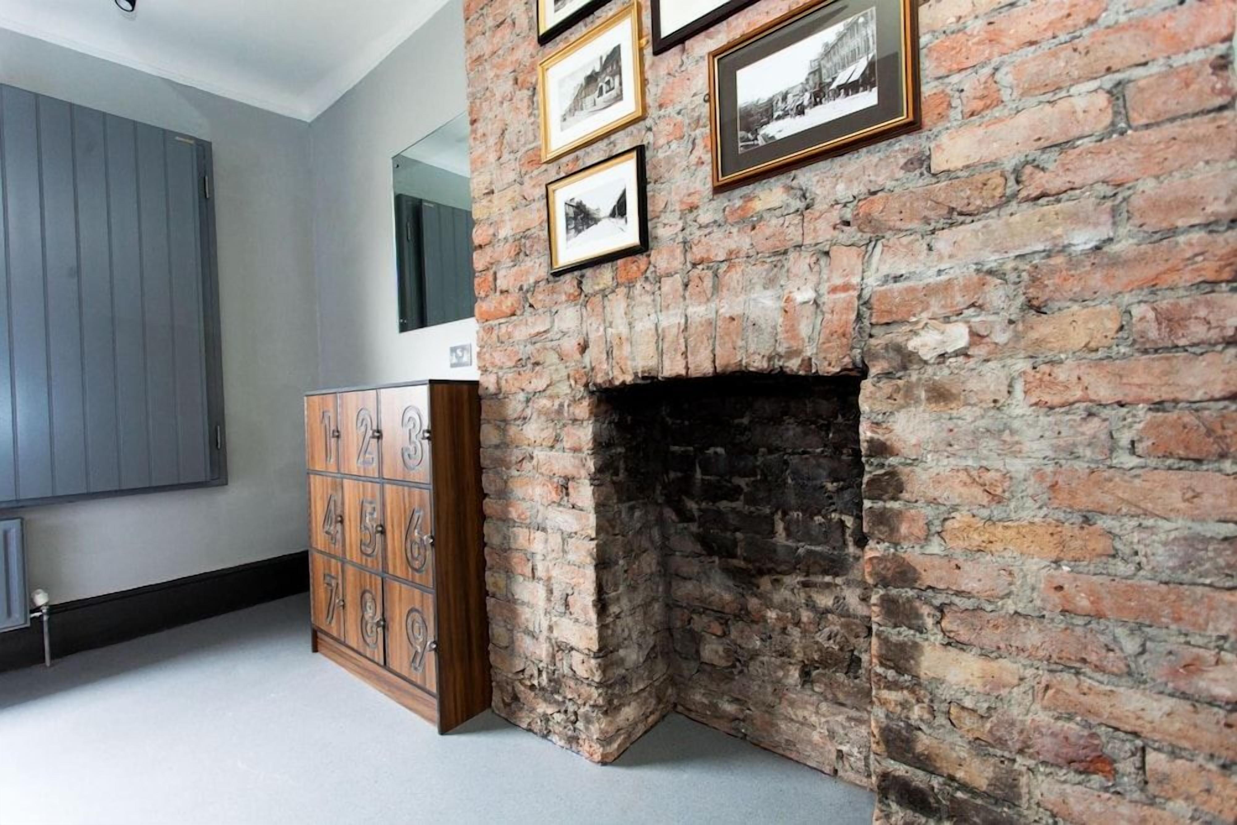 A room with a brick fireplace, a wooden cabinet with numbers, and framed pictures on the wall.