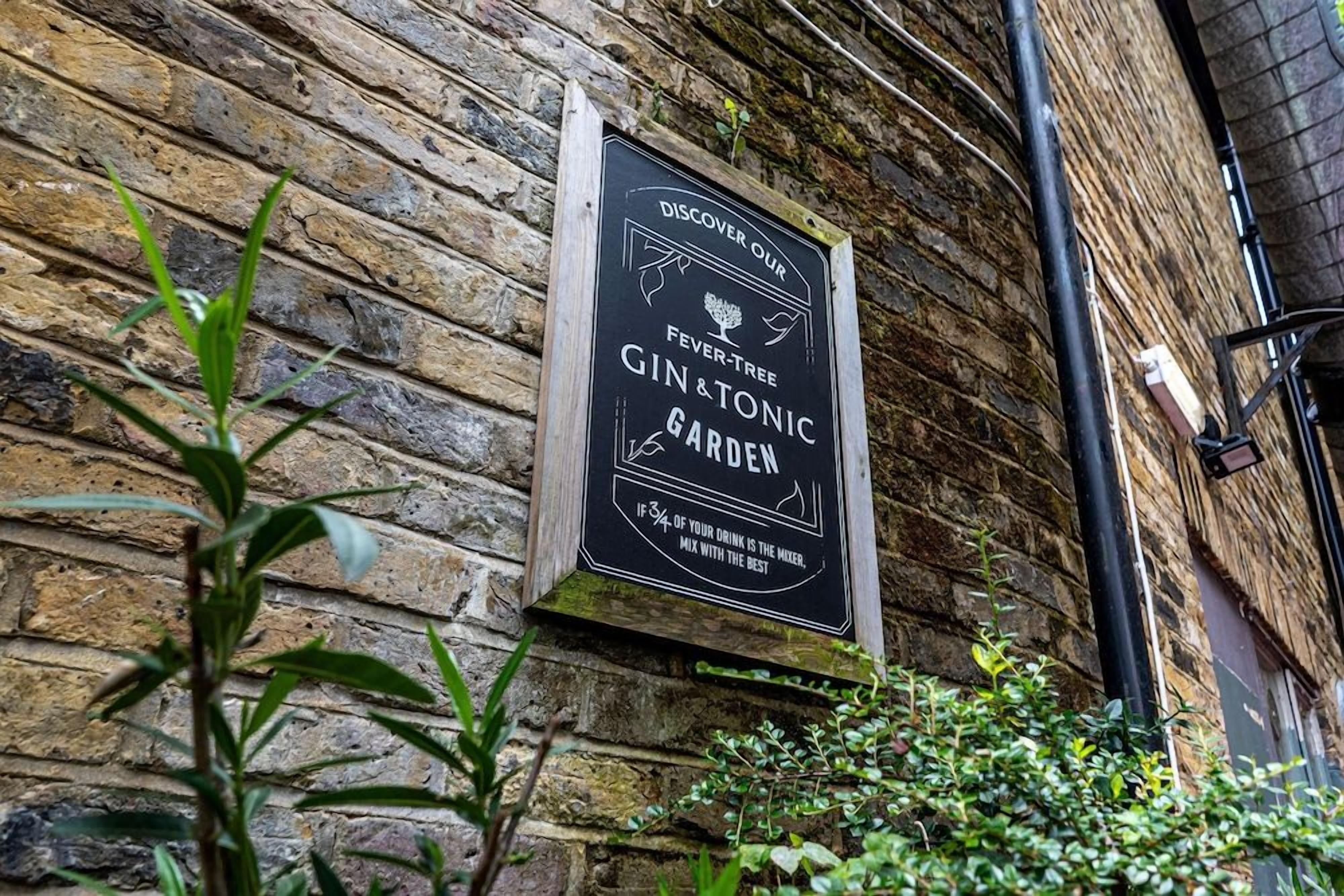 Un muro de ladrillo con un cartel anunciando un jardín de ginebra y tónica Fever Tree.