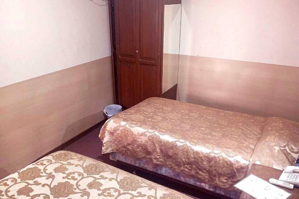 Habitación de hotel con dos camas, un armario de madera, un televisor montado en la pared y una mesita con un control remoto.