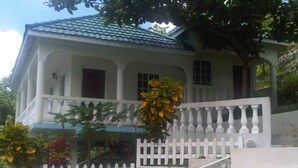 Uma casa de dois andares com fachada branca, telhado azul e guarda-corpo de varanda branco.