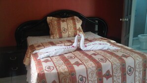 Cama bem arrumada com colcha estampada com flores e dois cisnes feitos de toalhas.