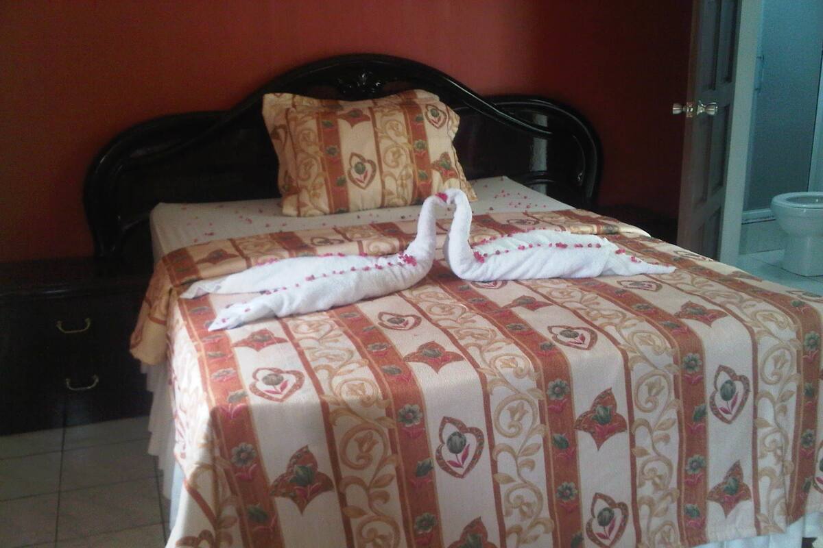 A neatly made bed with a floral-patterned bedspread and two swans made of towels.