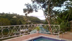 Uma piscina com grade de metal branca e vista para uma paisagem montanhosa ao fundo.