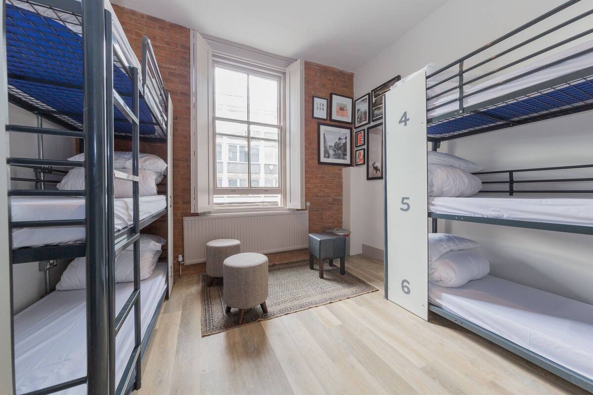 Une chambre de dortoir avec des lits superposés, une fenêtre, un radiateur et une petite table avec un tapis.