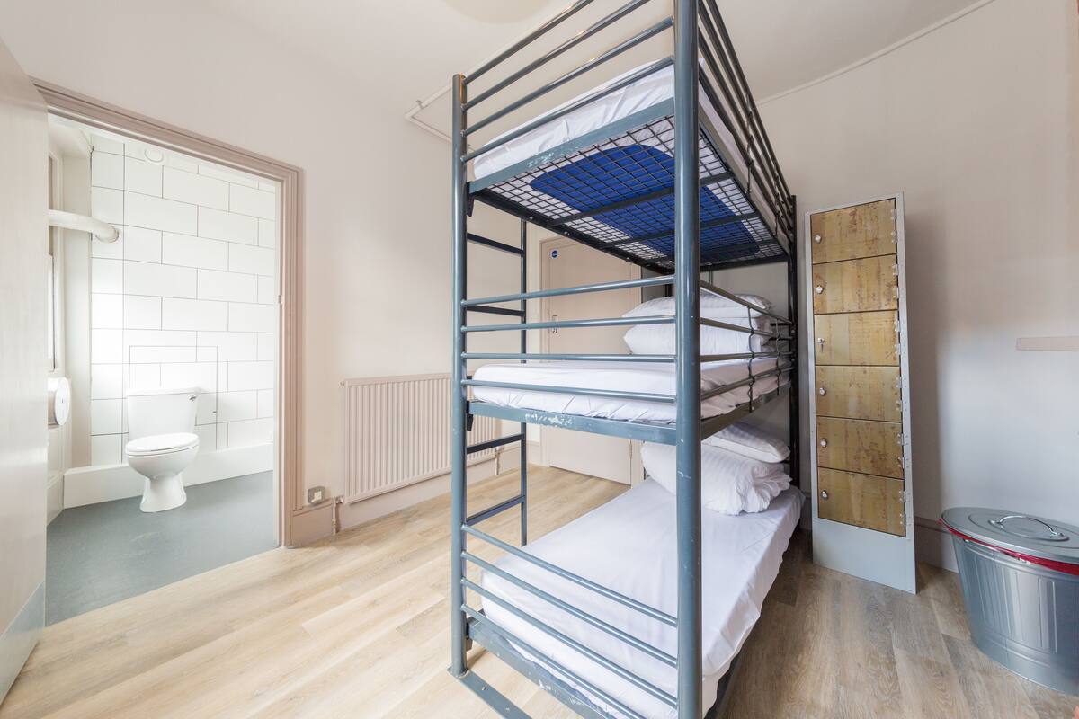 Une chambre avec un lit superposé, un plancher en bois, des toilettes blanches et un radiateur.