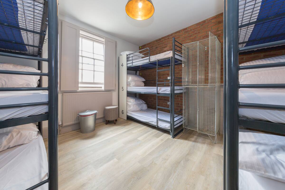 Une chambre de dortoir avec des lits superposés, une fenêtre, un radiateur et une poubelle.