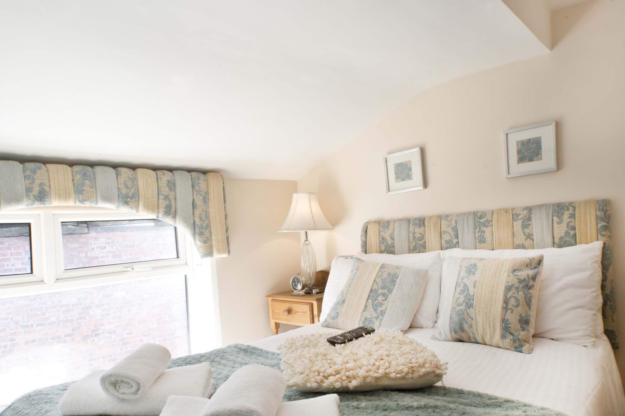 A hotel room with a bed, a nightstand, a lamp, and a window with curtains.