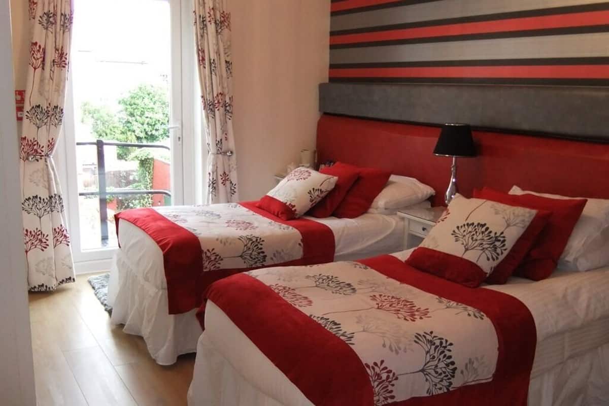 A hotel room with two beds, each with red and white bedding, a striped wall, and a window with curtains.
