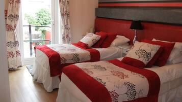 Habitación de hotel con dos camas, cada una con ropa de cama roja y blanca, una pared a rayas y una ventana con cortinas.