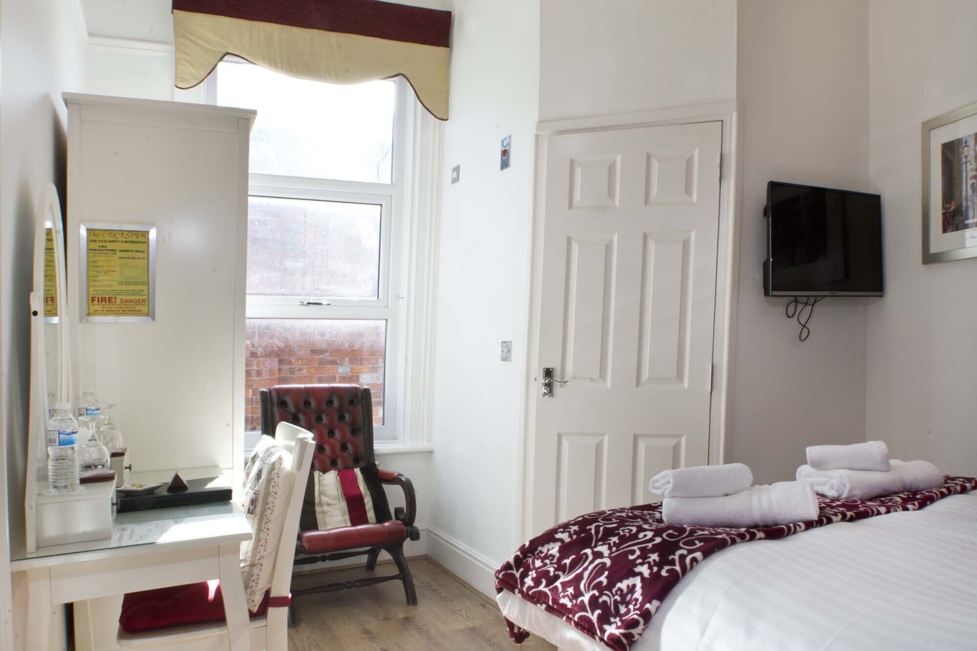 A hotel room with a bed, a chair, a desk with a computer, a television, and a window with a view of a brick building.