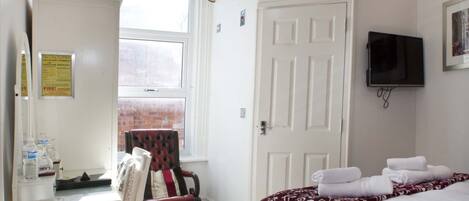 A hotel room with a bed, a chair, a desk with a computer, a television, and a window with a view of a brick building.