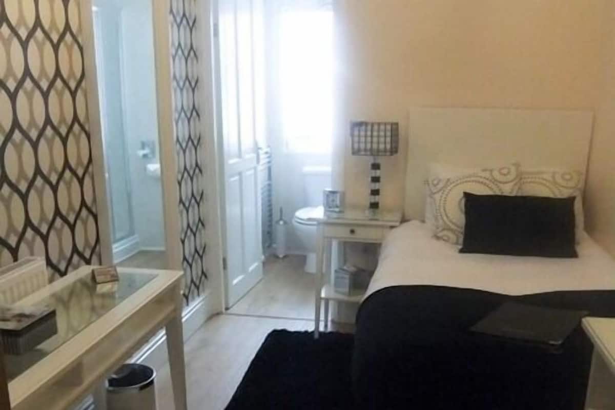 A hotel room with a bed, bedside table, and a desk with a lamp.