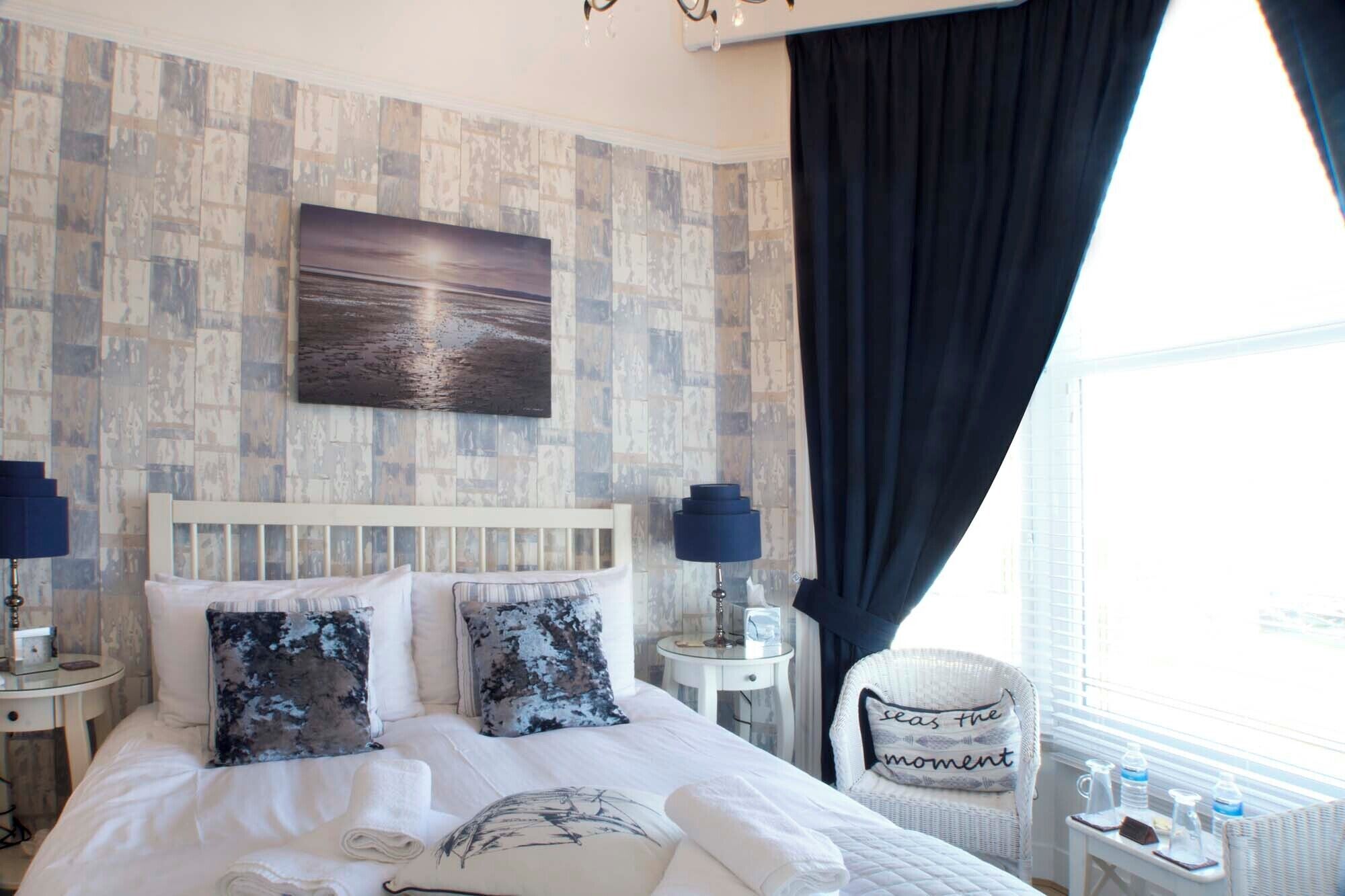 A hotel room with a large bed, two bedside tables, a chair, a view of the city, and a painting on the wall.