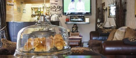 A living room with a glass display case containing pastries, a television, and a bar area in the background.