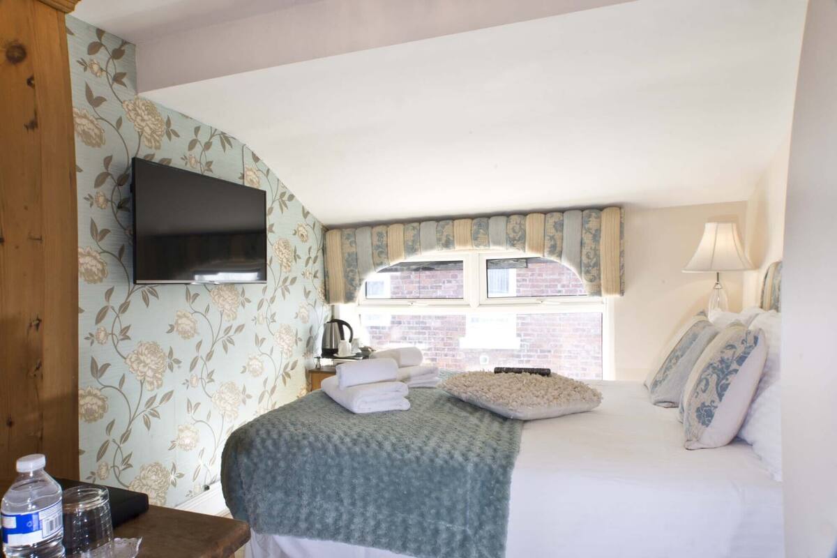 A hotel room with a bed, a flat-screen TV, a window with curtains, a lamp, and a view of a brick building.