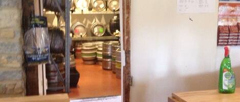 A kitchen with a wooden counter, a green bottle, and a door leading to a room with shelves and jars.