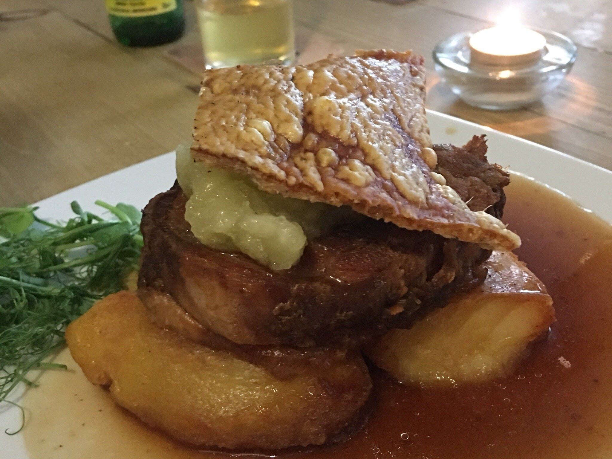 A plate of food with a piece of meat, potatoes, and a garnish.