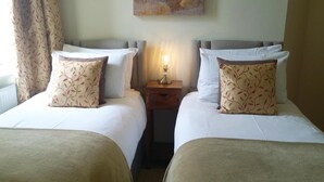 A hotel room with two single beds, each with a matching pillow and a bedside table with a lamp. - The Cross Keys Inn (Somerton)