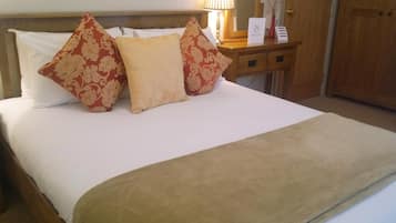 Una cama bien hecha con almohadas de estampado floral, una mesita de noche con lámpara y una puerta de madera al fondo.