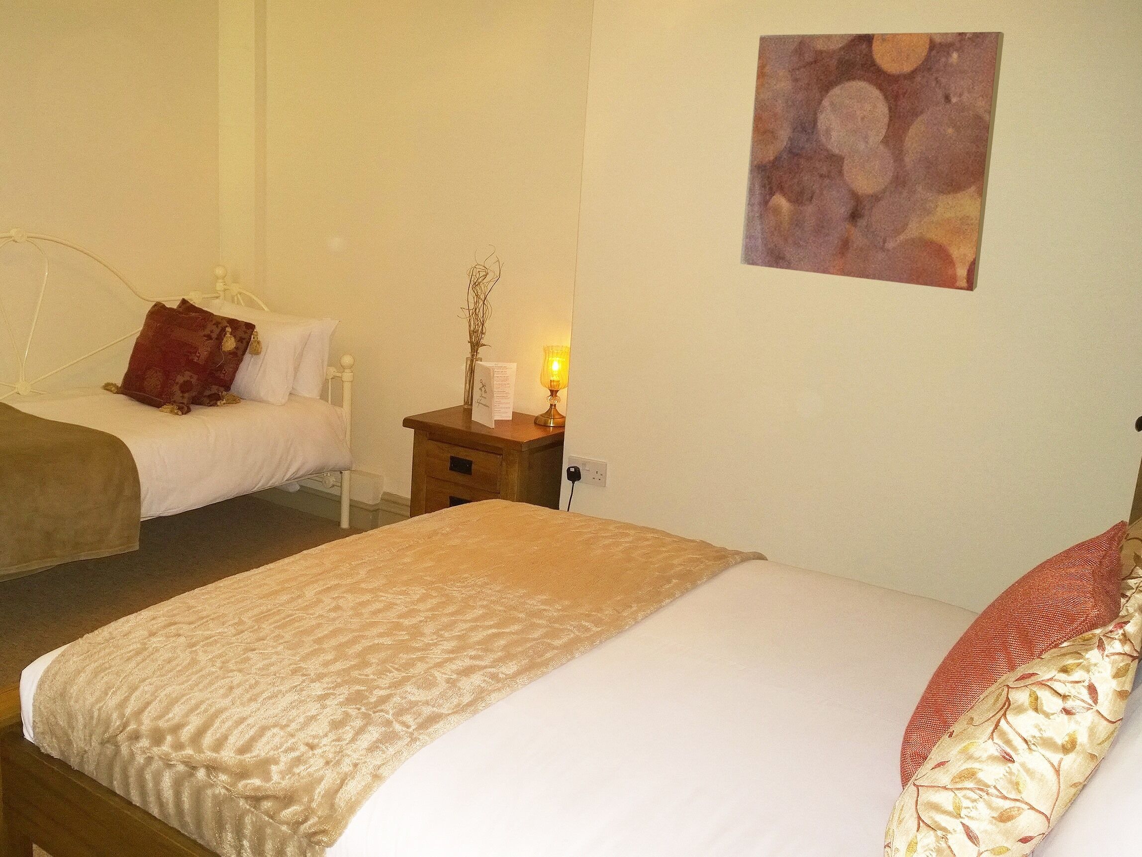 A hotel room with two single beds, a nightstand with a lamp, and a wall-mounted artwork.