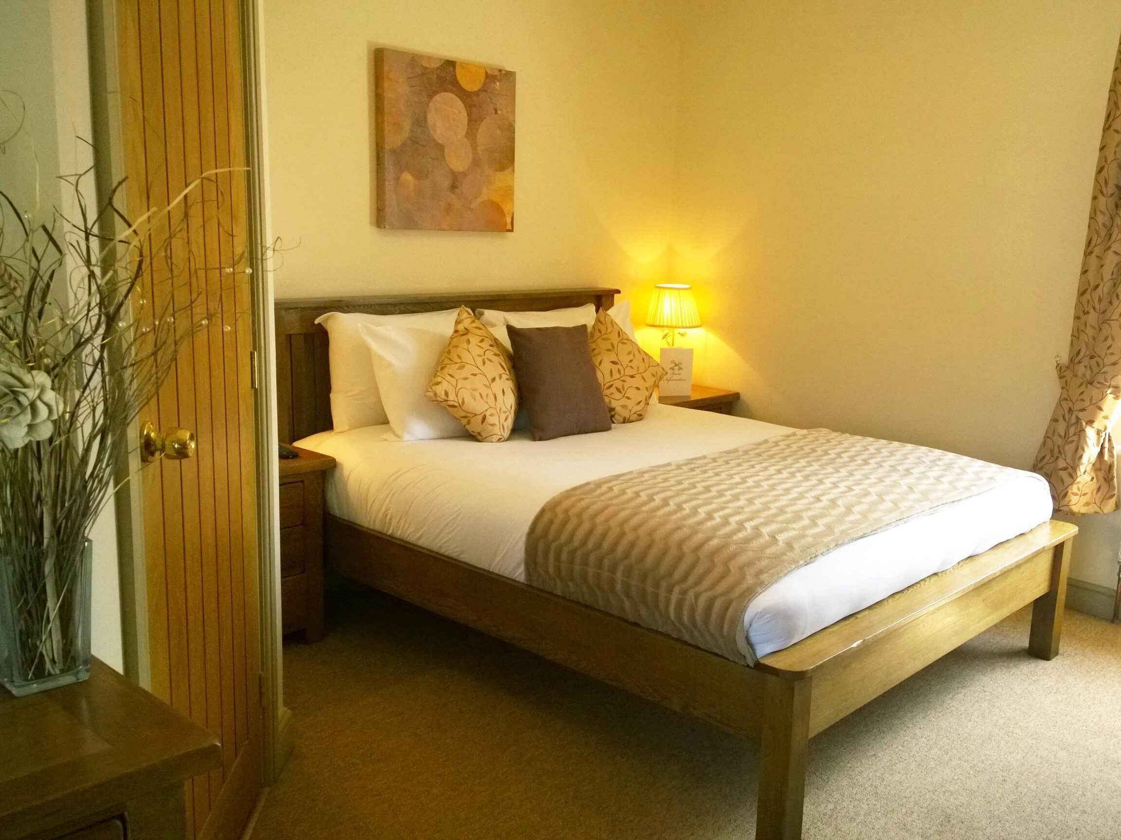 Een net opgemaakt bed met houten frame, een bedlampje en een wanddecoratie.