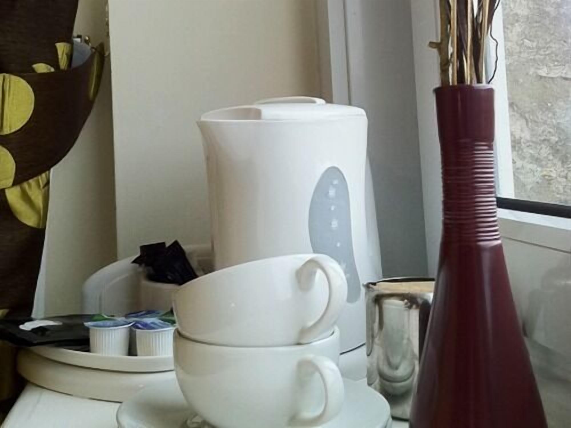 Una cocina con cafetera, un florero y una bandeja con tazas y platos.