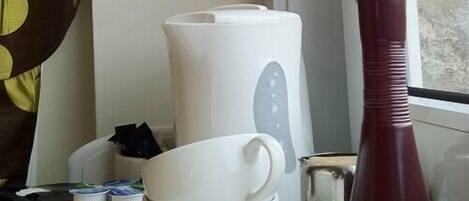 Una cocina con cafetera, un florero y una bandeja con tazas y platos.