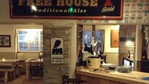 A bar area with a 'Free House' sign, a 'No Gates' sign, and a rustic interior with stone walls and wooden furniture. - The Cross Keys Inn (Somerton)