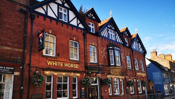 Um pub tradicional chamado "White Horse", com fachada clássica em estilo Tudor, apresentando estrutura de madeira aparente e revestimento de tijolos.
