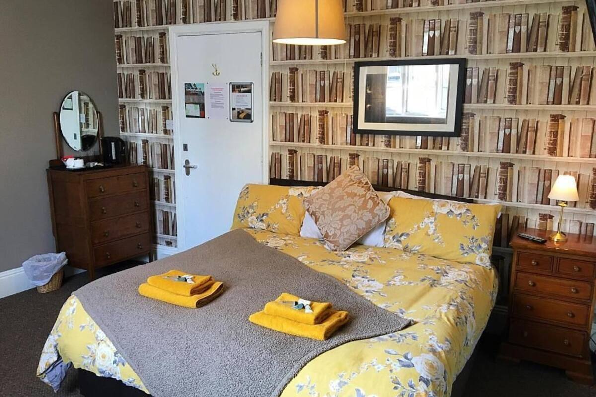 A bedroom with a bed, a dresser, a mirror, and a bookshelf filled with books.