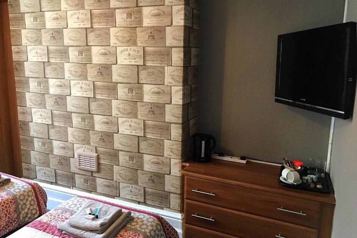 A hotel room with a brick-patterned wall, a flat-screen TV, a wooden dresser with a tray of toiletries, and a window with a view.