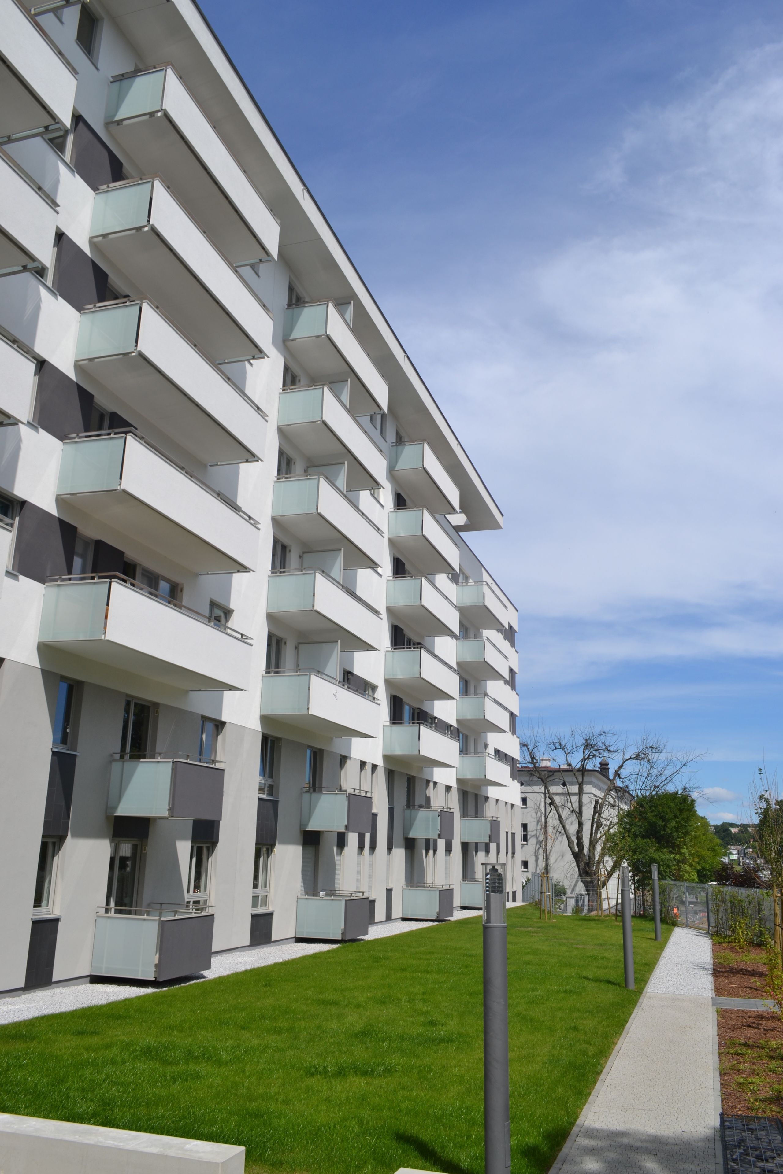 Ein modernes Mehrfamilienhaus mit Balkonen, einem gepflegten Rasen und blauem Himmel.