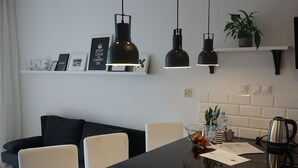 Een moderne keuken met een zwart aanrecht, witte kasten en hanglampen. Er is een zithoek met een zwarte bank en witte stoelen.