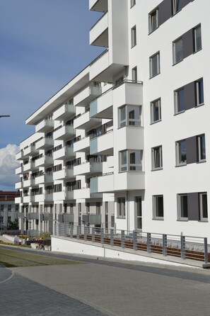 Un immeuble moderne à plusieurs étages, doté de balcons, d’un toit plat et d’un rez-de-chaussée pavé.