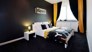 Een moderne hotelkamer met een groot bed, een nachtkastje met een lamp, een raam met gele gordijnen en een schilderij aan de muur.