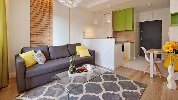 Een moderne woonkamer met een grijze bank, een glazen salontafel en een kamerbreed tapijt met dessin.