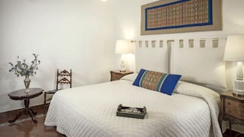 A neatly arranged bedroom with a large bed, a bedside table, a chair, a lamp, and a wall art piece.