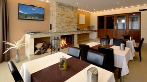 Un comedor con mesas dispuestas para invitados, una chimenea encendida y un televisor montado en la pared.