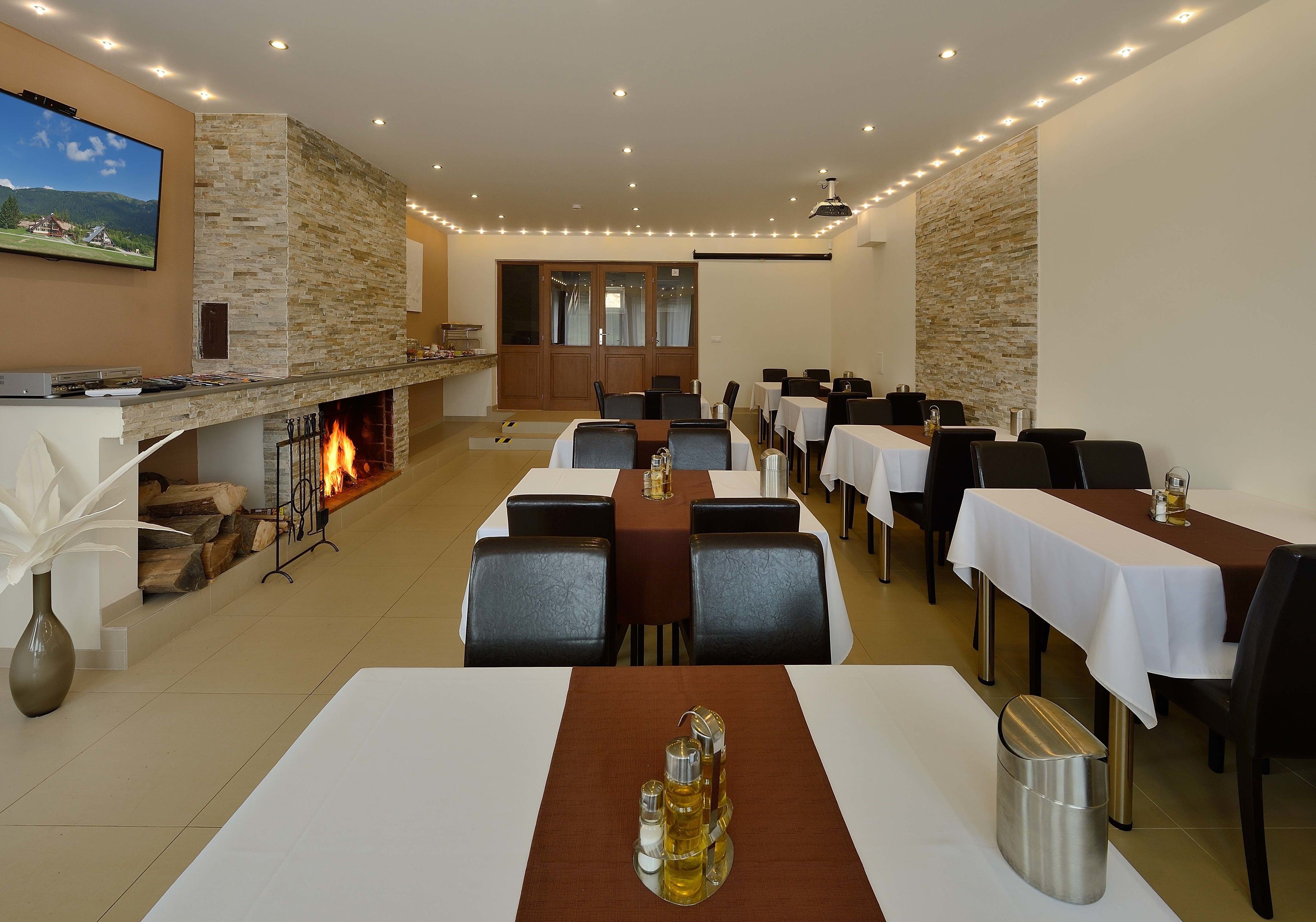 A dining area with tables set for guests, a fireplace, and a television mounted on the wall.