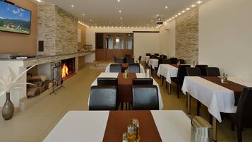 A dining area with tables set for guests, a fireplace, and a television mounted on the wall.