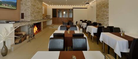 A dining area with tables set for guests, a fireplace, and a television mounted on the wall.